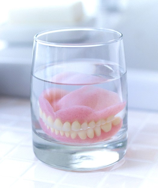 Dentures in Pewaukee soaking in glass on bathroom countertop