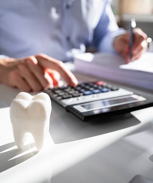 Person using calculator sitting next to model of a healthy tooth
