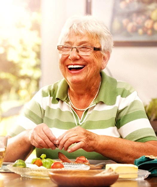Woman at dinner table smiling with dentures in Pewaukee