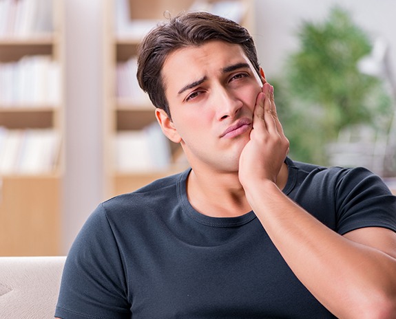 Young man in need of wisdom tooth removal holding jaw