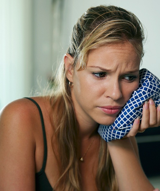 Woman in need of wisdom tooth extraction holding ice pack to cheek