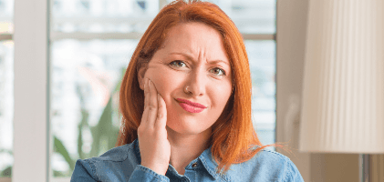 Woman in need of restorative dentistry holding cheek