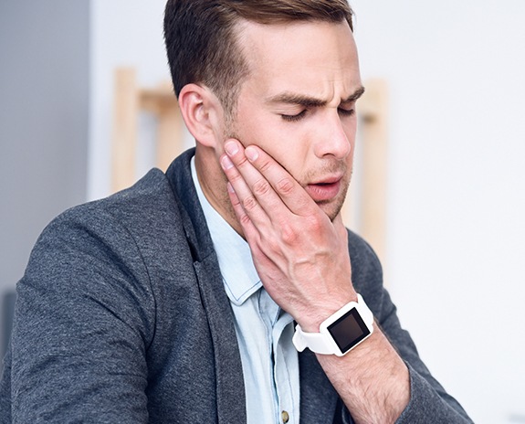 Man in need of T M J therapy holding jaw in pain